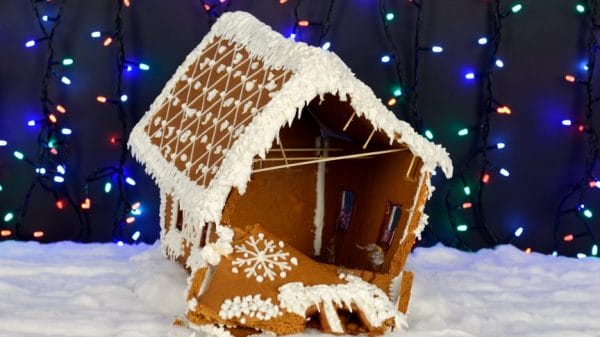 Crumbling gingerbread house in front of a backdrop of Christmas lights.