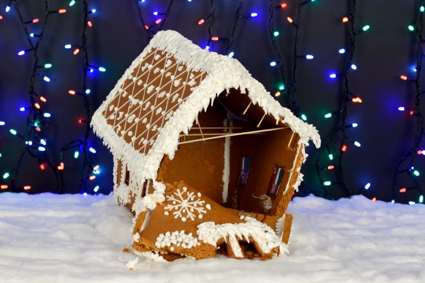 Crumbling gingerbread house in front of a backdrop of Christmas lights.