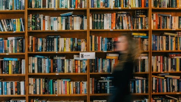 Blurry picture of a girl walking by a wall-length bookshelf, meant to represent the BookTok community.