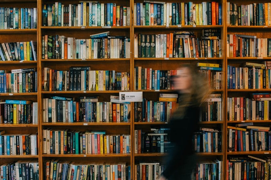 Blurry picture of a girl walking by a wall-length bookshelf, meant to represent the BookTok community.