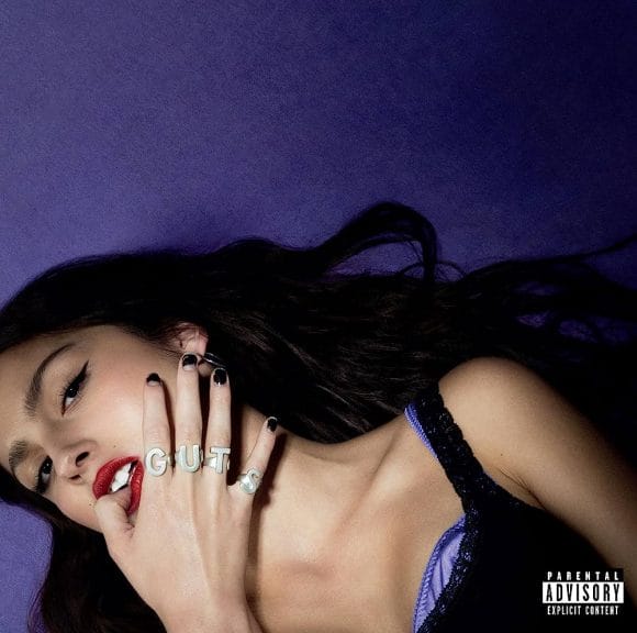Album cover for GUTS, Olivia Rodrigo in a black top on a purple background. Each ring on her finger reads out GUTS.