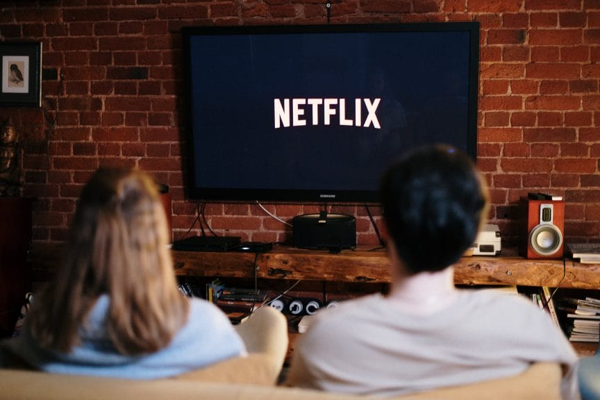 Two people sitting on the couch in front of a TV with the Netflix logo on the screen.