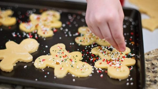Person decorates gingerbread-shaped sugar cookies with sprinkles.