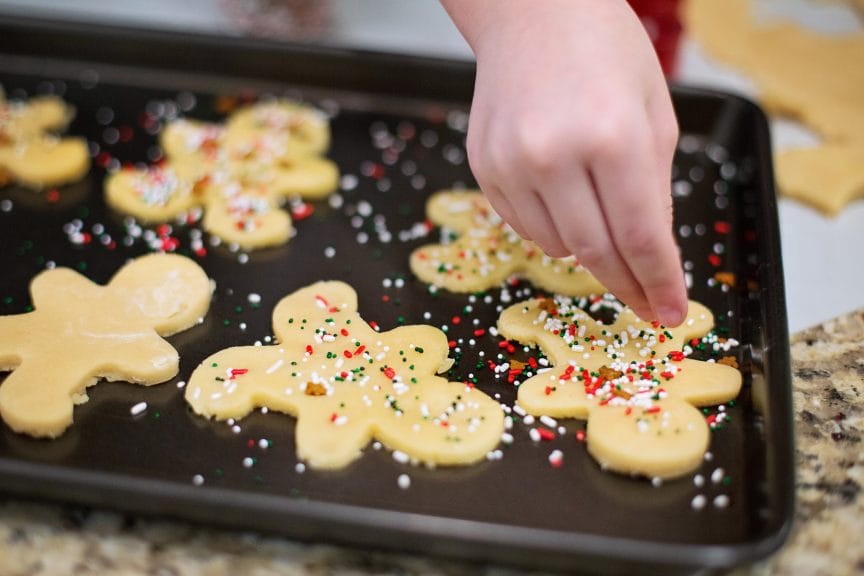 Person decorates gingerbread-shaped sugar cookies with sprinkles.
