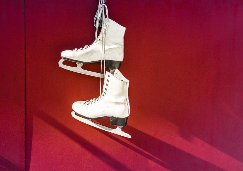 Pair of white ice skates in front of red background.