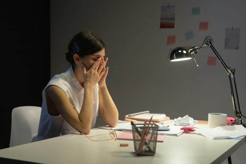 Stressed out woman rubbing her eyes while sitting at a desk. 