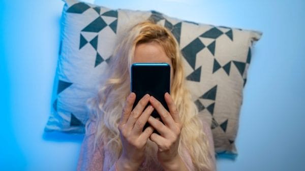 Woman lying in bed holding phone in front of her face while scrolling