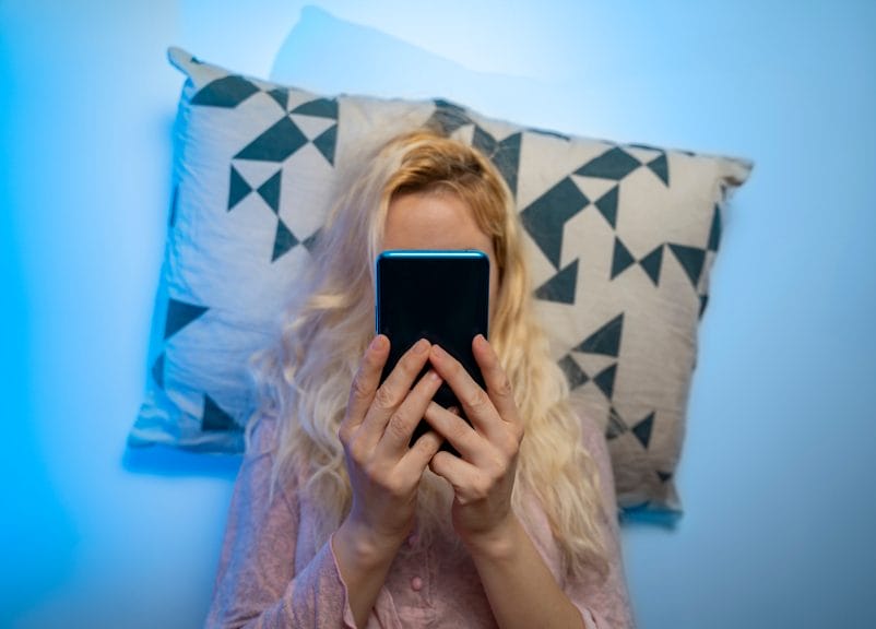 Woman lying in bed holding phone in front of her face while scrolling