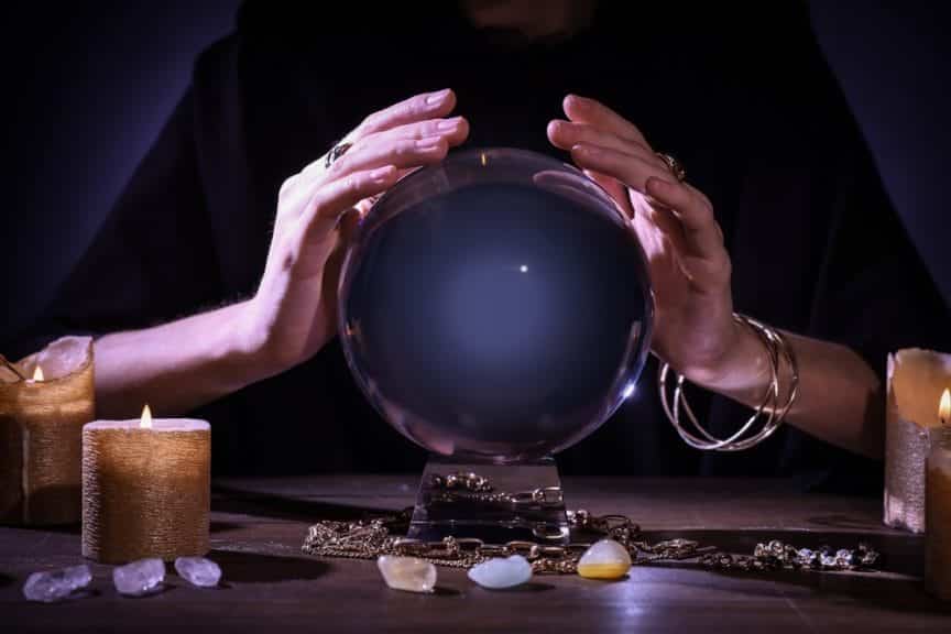 Soothsayer using crystal ball to predict future at table in darkness, closeup.