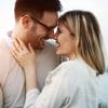 A man and woman in a relationship stand with their faces close together. They are smiling, about to kiss.