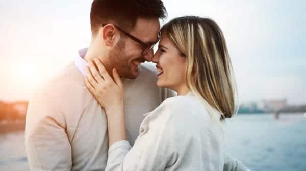 A man and woman in a relationship stand with their faces close together. They are smiling, about to kiss.