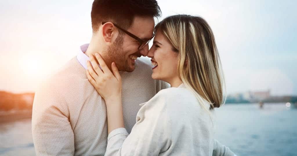 A man and woman in a relationship stand with their faces close together. They are smiling, about to kiss.