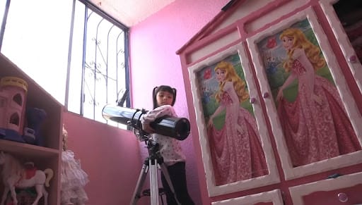Still of Adhara in her pink room hugging her telescope