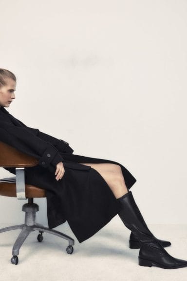 model in chair wearing black trench coat and calf length black boots from ZARA