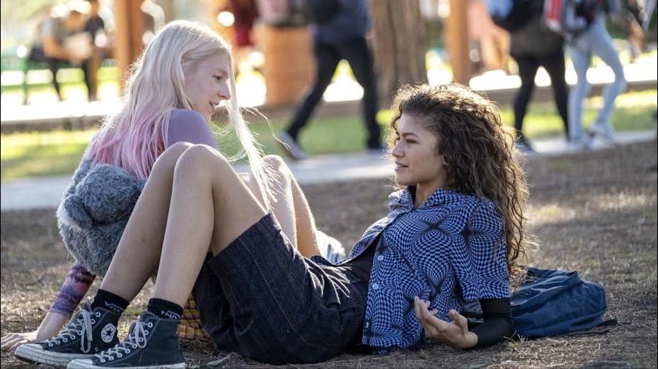 Two teenage girls laying on the ground and having a conversation.