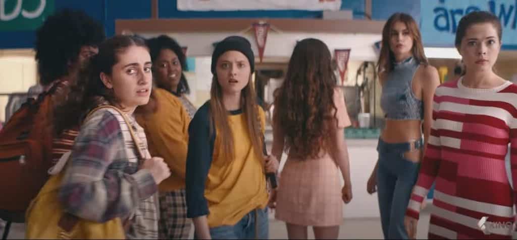 A group of young women in varying outfits look at the camera in shock