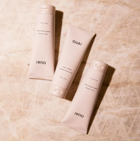3 Ouai Curl Cream containers on a pink background.
