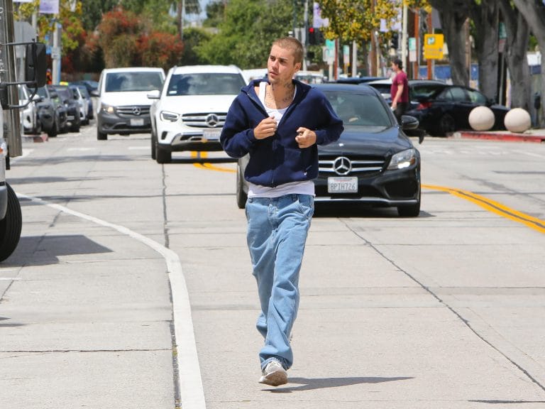 Justin Bieber out for a jog in Los Angeles. He is wearing a dark blue zip-up hoodie and light blue jeans. 