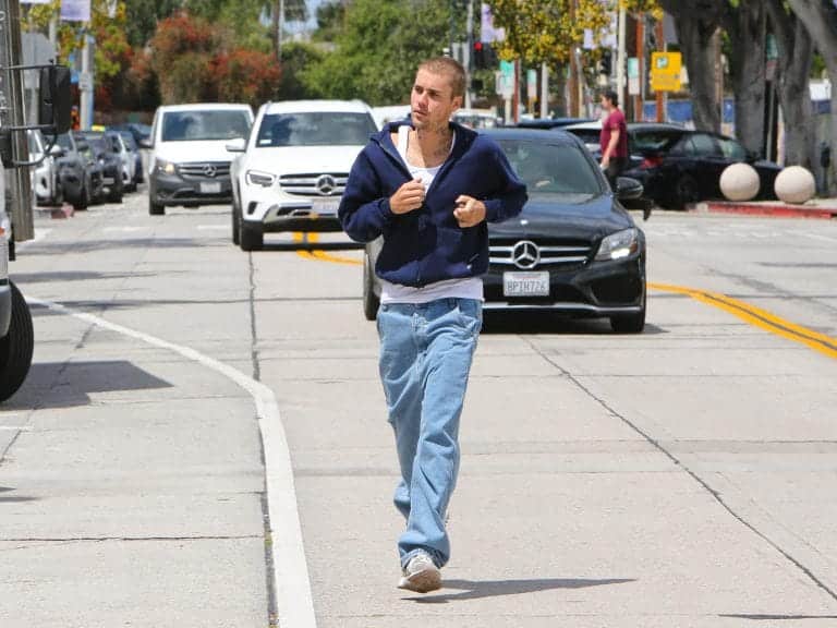 Justin Bieber out for a jog in Los Angeles. He is wearing a dark blue zip-up hoodie and light blue jeans.