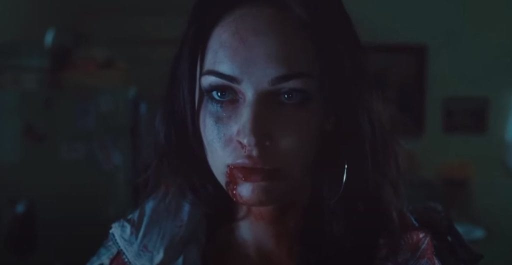 Jennifer, a woman with black hair and pale skin stands with blood dripping from her mouth