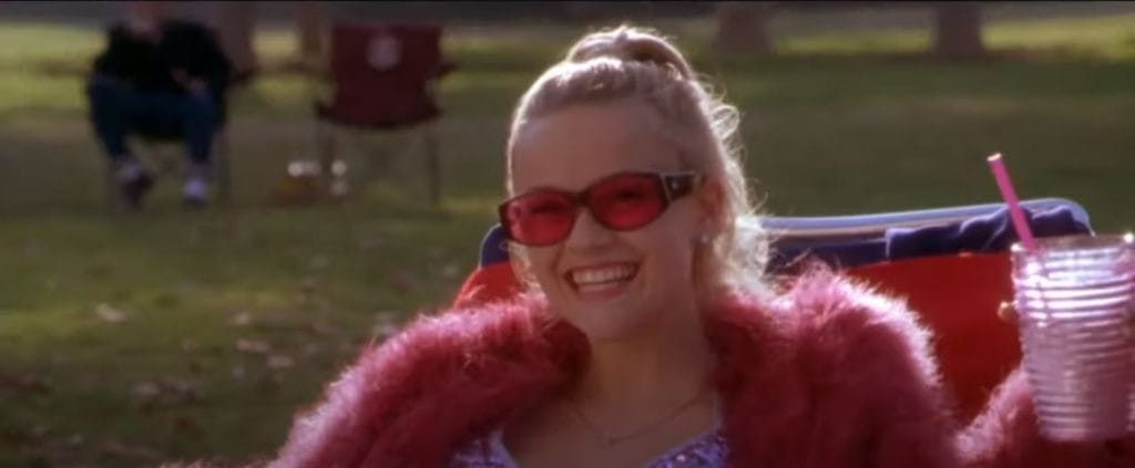 Elle Woods, a girl with blonde hair wearing pink and sunglasses smiles brightly