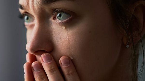 Woman with her hands covering her face with a tear rolling down.