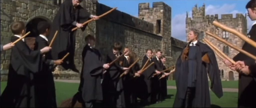 A group of robed students stand on broomsticks