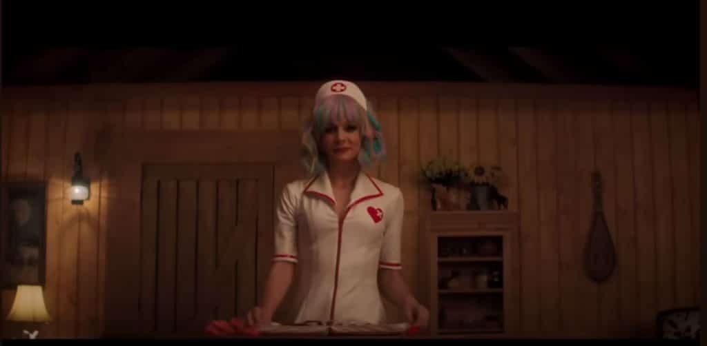 Cassie, a woman wearing a rainbow wig and a nurses costume, stands in front of a table of medical equipment