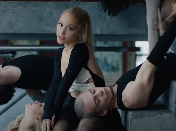 Ariana Grande sitting on stairs surrounded by dancers in new music for her single, "yes, and?"