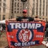 trump supporter holding a homemade flag that reads "Trump or Die" with the years "1776" and "2024" on either side.