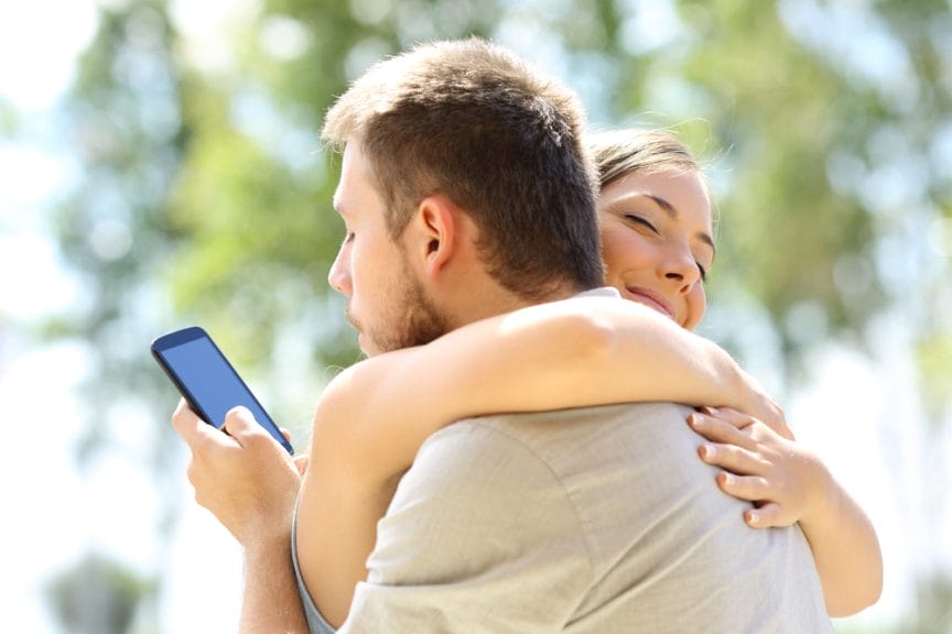 A man is on his phone while hugging his girlfriend.