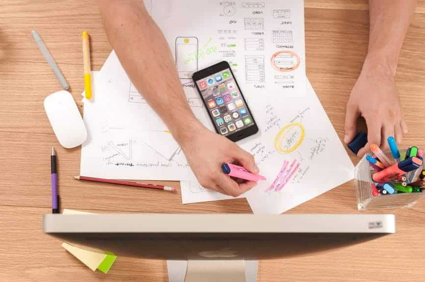 Overhead view of a person at a desk on their phone and laptop while writing 