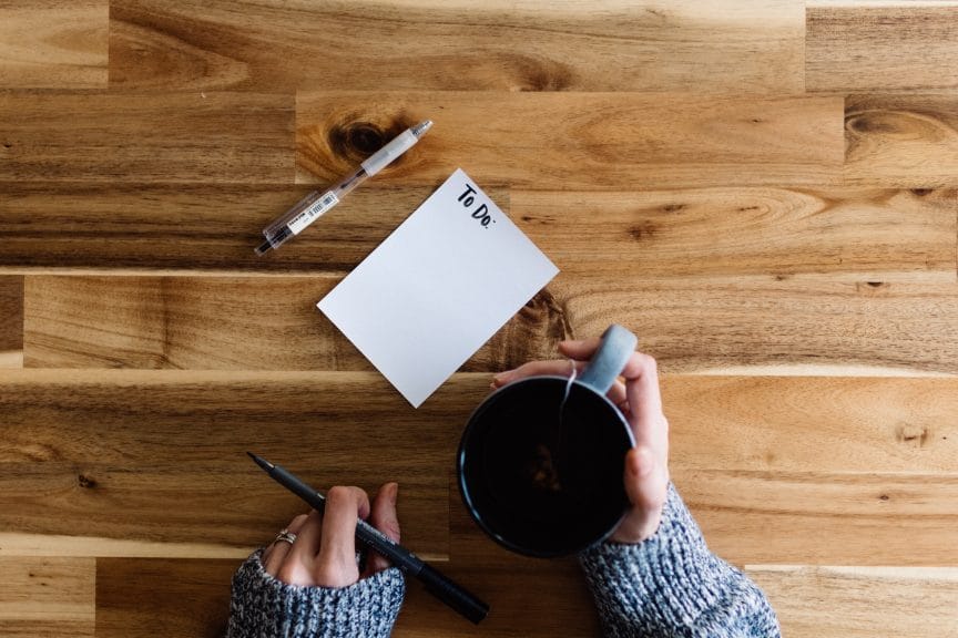 Aerial view of girl sitting at table with to-do list and cup