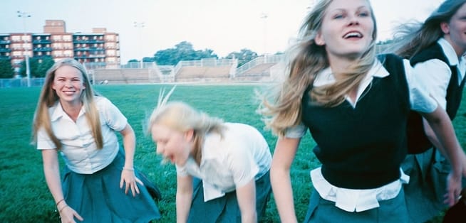 Four blonde girls playing on a field in their school uniforms.