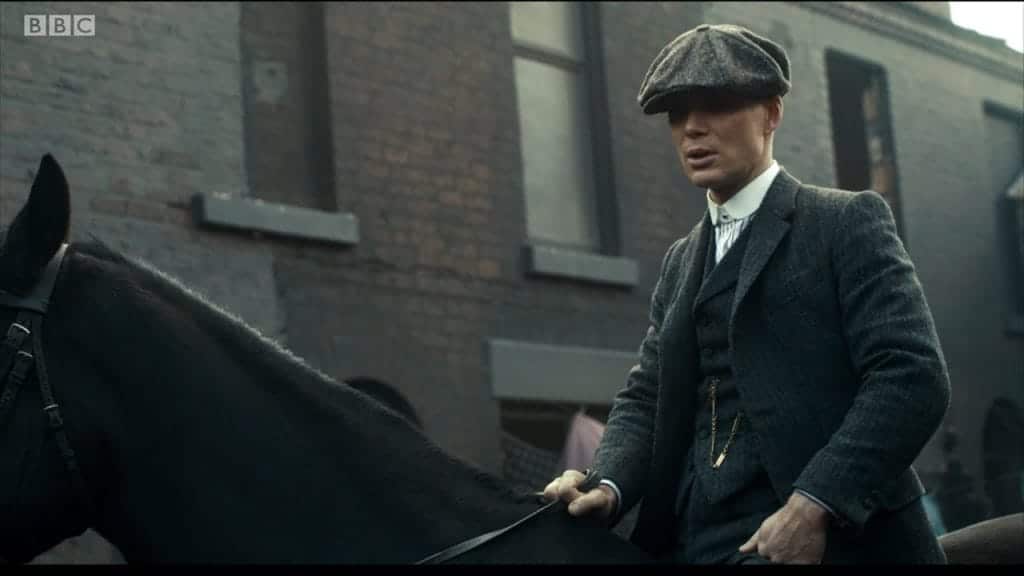 A white man in a flat cap and suit riding a horse