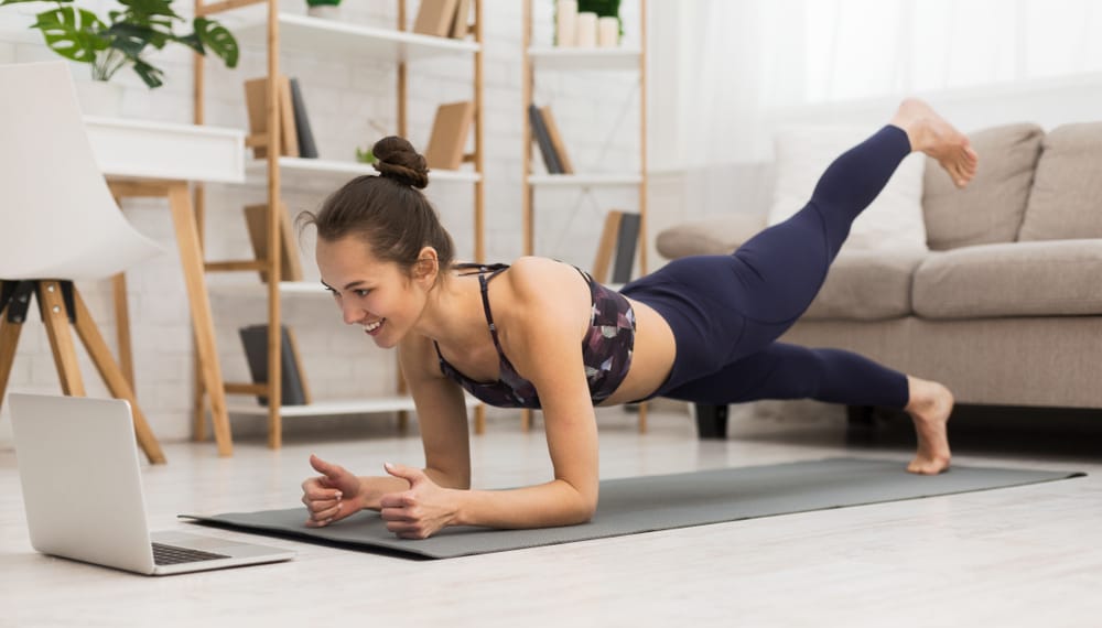 woman doing yoga plank and watching online tutorials on laptop, training in living room
