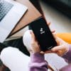 Woman holding iPhone with TikTok app logo on the screen and computer in the background