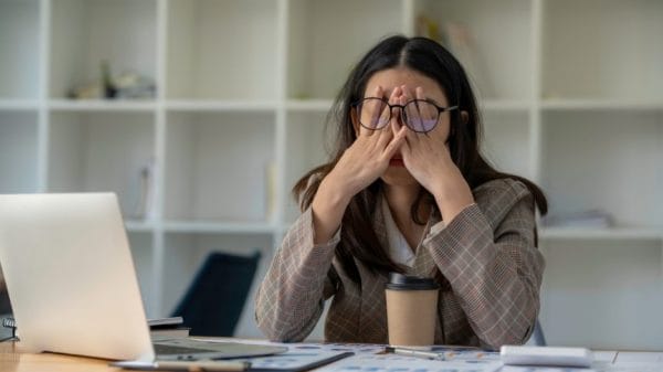 Overwhelmed girl at desk behind computer rubbing her face