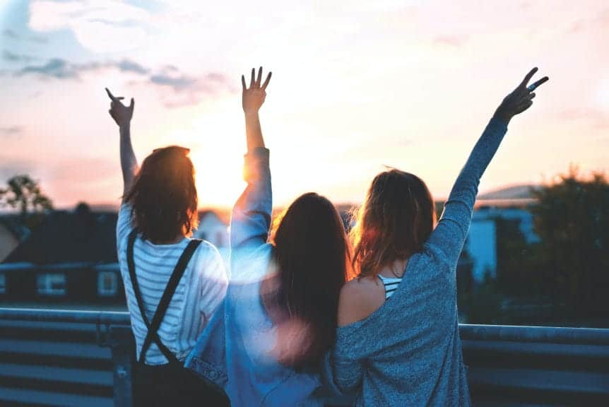 Three young girls looking off towards a sunset