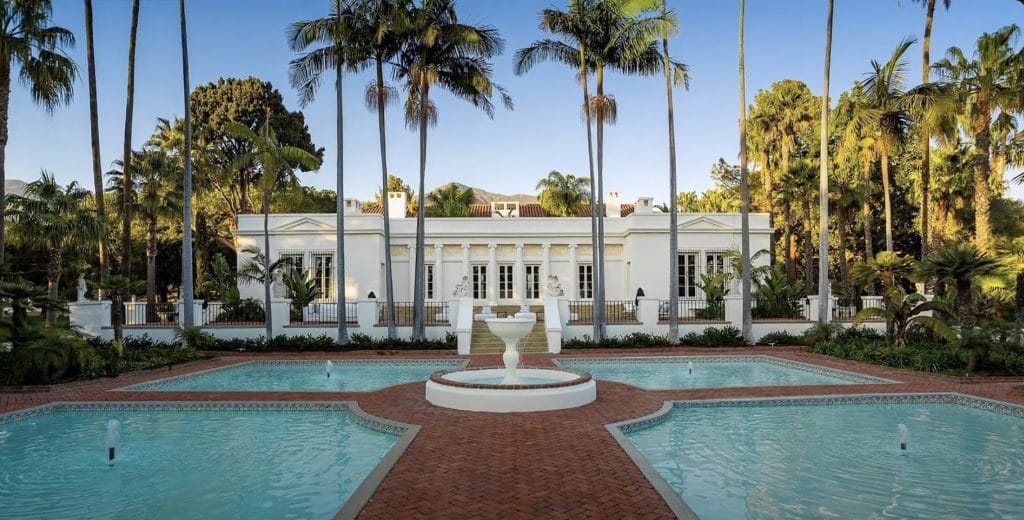 A white house with four illars in fron of a four sides of water with a fountain in the middle.
