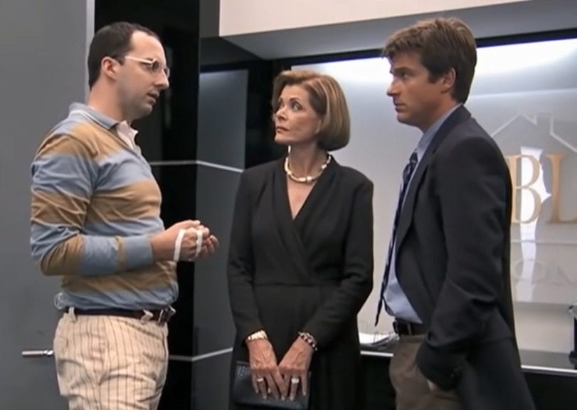 Three of the members of the Bluth family stand in the office of the family business, engaged in discussion. 