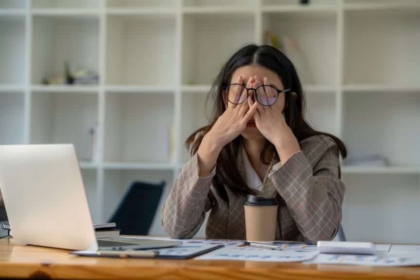 Stressed girl rubbing her eyes sitting in front of her laptop and a cup of coffee.