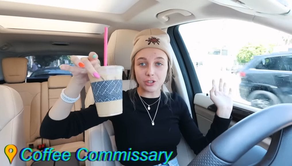 Emma Chamberlain sitting in her car, showing a cup of coffee to the camera.