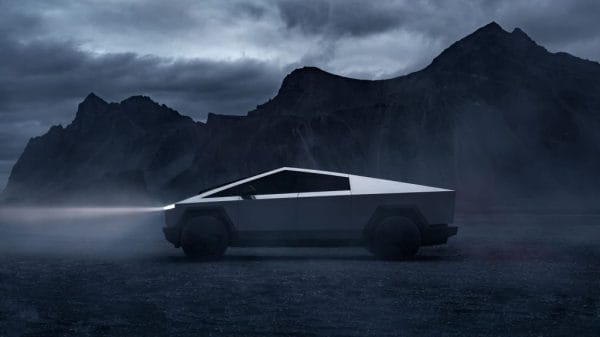 A metal triangle-shaped vehicle shining its headlights with dark mountains in the background