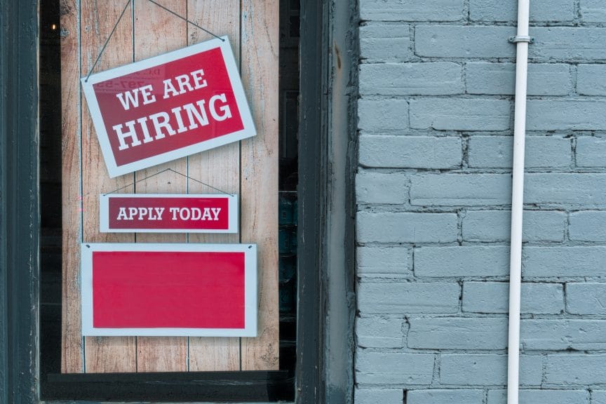 red "we're hiring sign" hanging outside of building