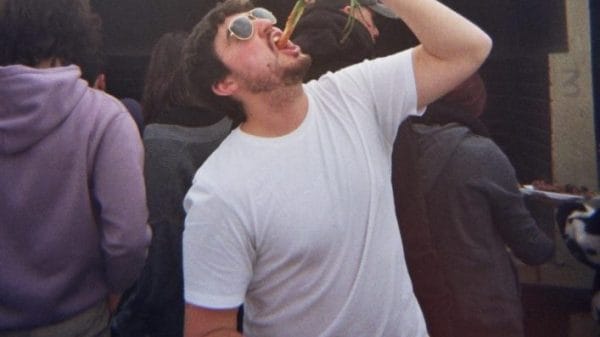 A man eating a calçot in a white t-shirt.