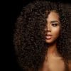 A black woman with long natural hair against a black background.