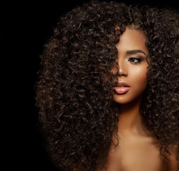 A black woman with long natural hair against a black background.