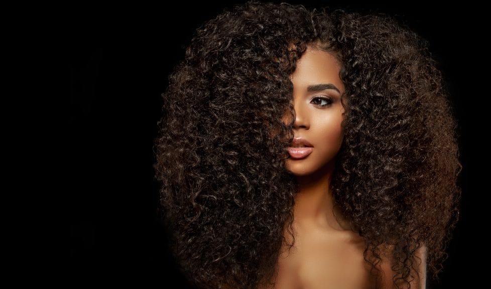 A black woman with long natural hair against a black background.