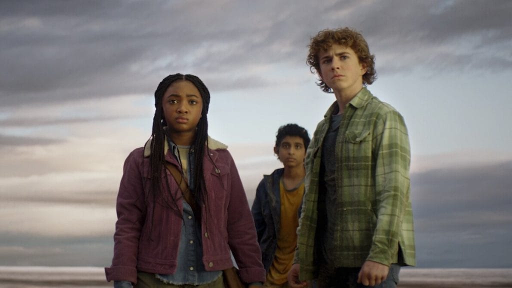 From left to right: Leah Sava Jeffries as Annabeth Chase, Aryan Simhadri as Grover Underwood and Walker Scobell as Percy Jackson. Stood against a dark background and looking in the direction of the camera. 